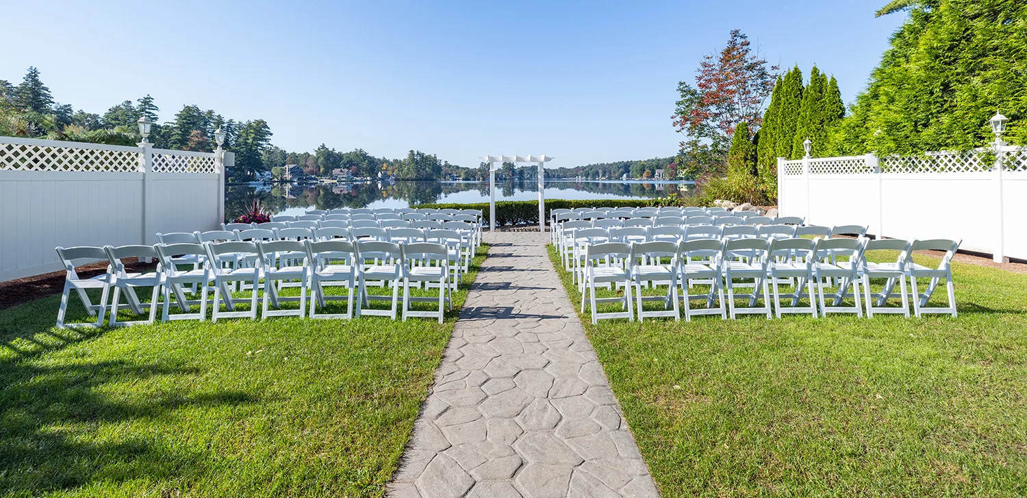 rows of chairs lined up in front of an alter on green grass with a lake in the background