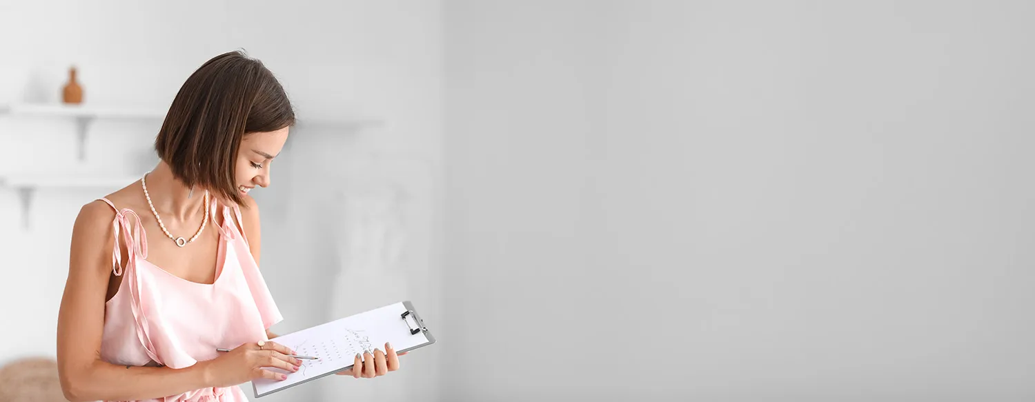young woman standing in a white room smiling at the paperwork she is holding