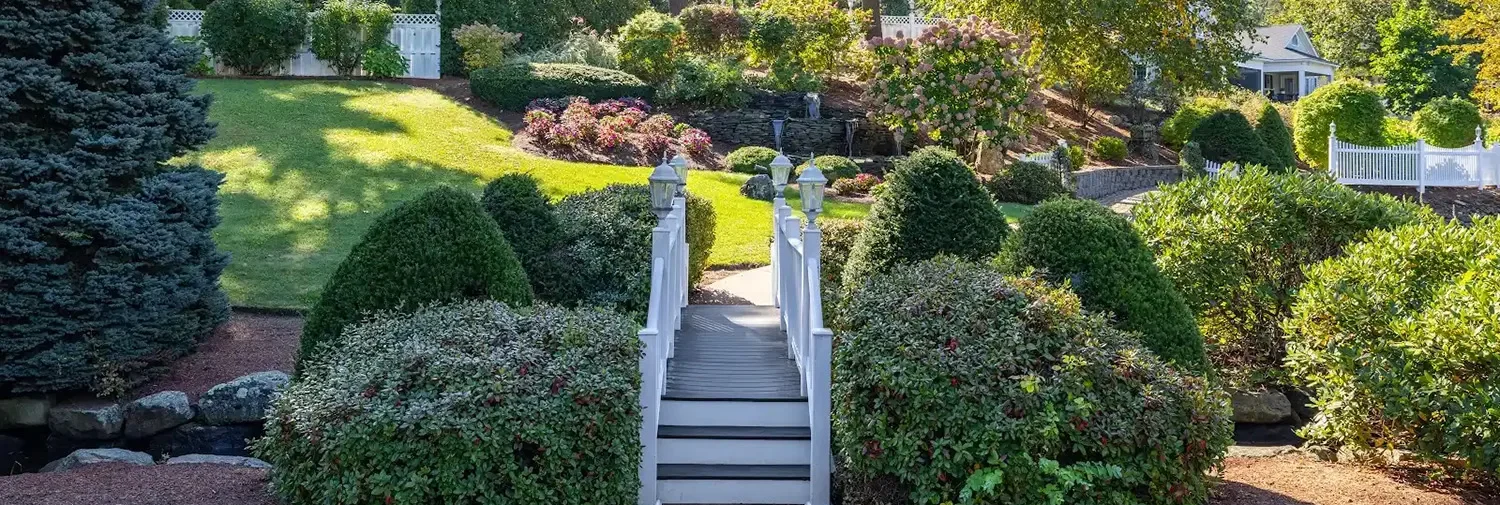 rustic wooden bridge crossing a stream surrounded with professional landscaping