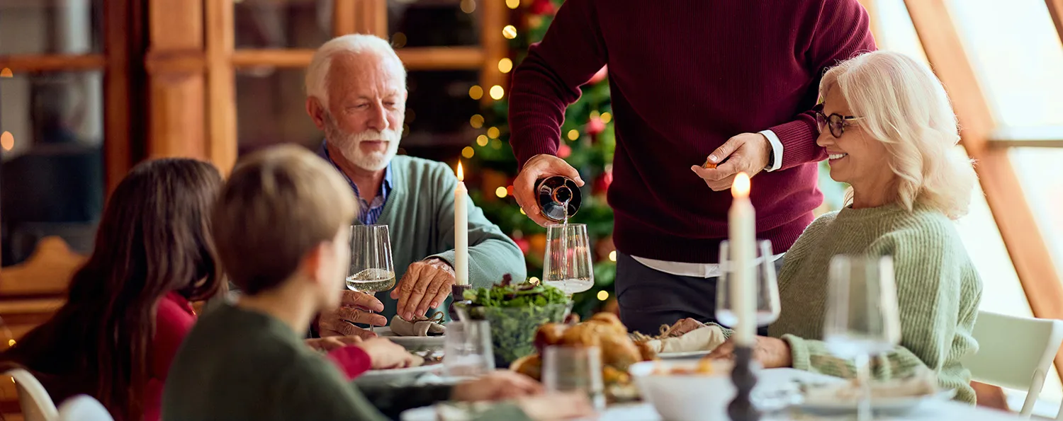 dad pours wine for grandpa while the whole family sits around a table decorated for Christmas