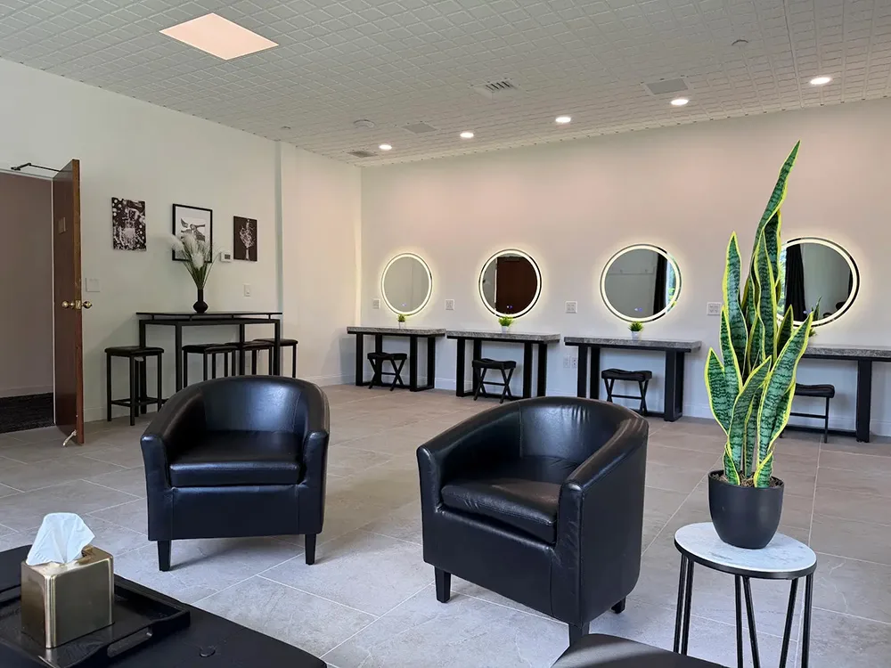 two leather chairs sit in the middle of the dressing room with the vanity mirrors and stations in the background