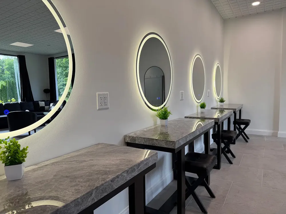 vanity mirrors mounted above small tables with chairs for makeup and hair styling