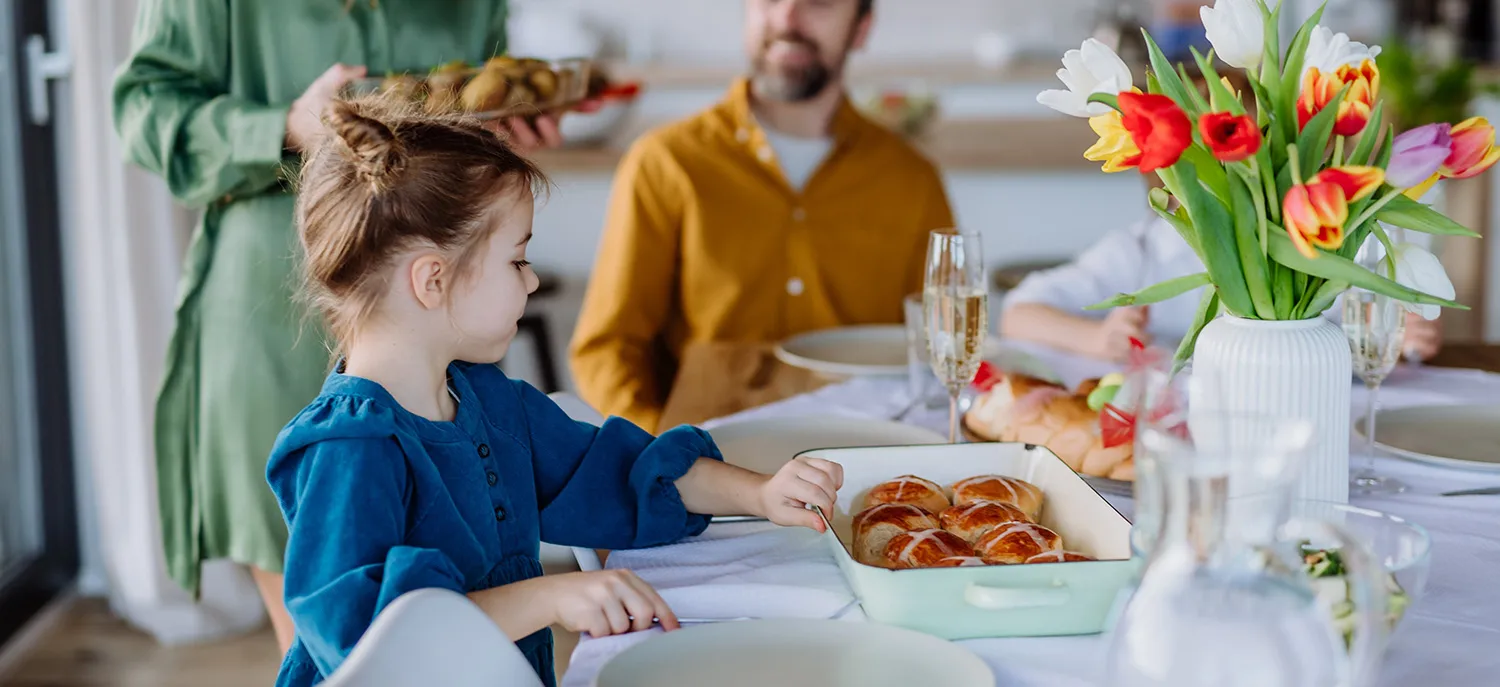 girl child sitting next to her father at a dinner table reaches for a pastry while mom serves dinner