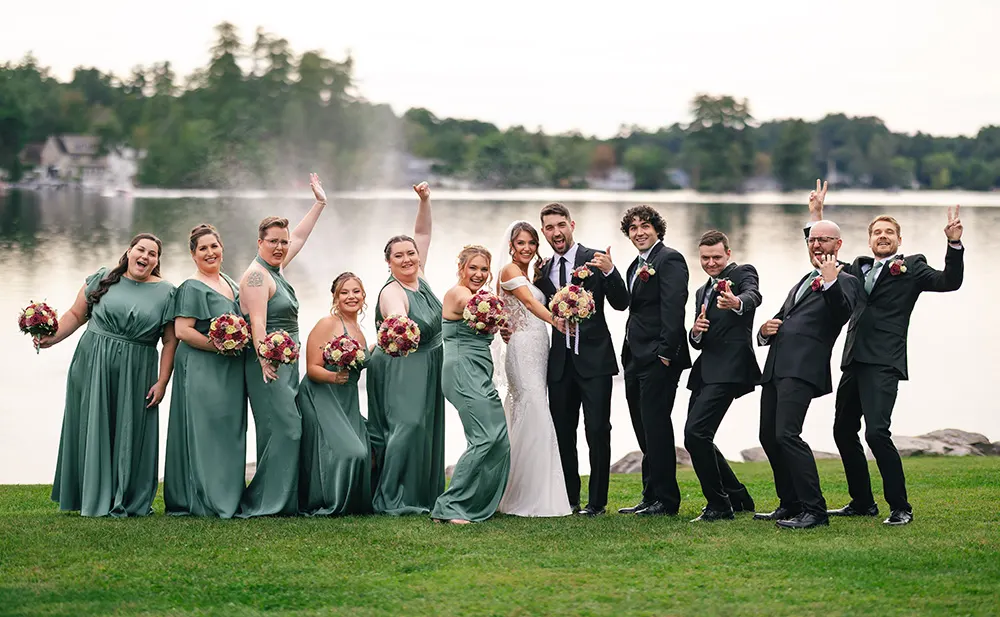 the whole wedding party doing silly poses next to the lake